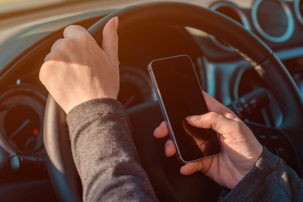 driving car while text messaging on mobile phone, hand holding smartphone and vehicle steering wheel, selective focus